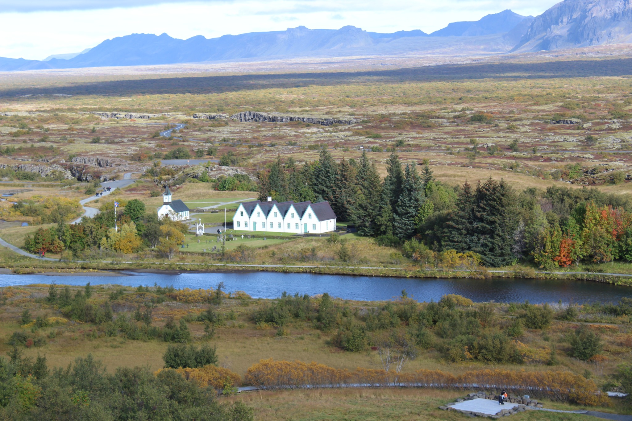 White buildings beside a river amid an expansive Icelandic landscape, with distant mountains.