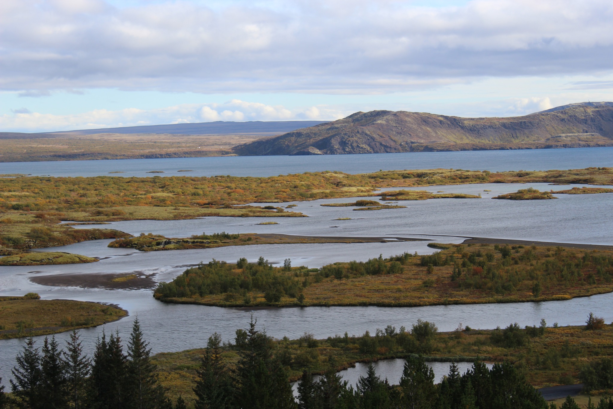 Winding waterways around low green islands, with a lake and distant hills beneath a blue-gray sky. Photograph by Janet Nash.